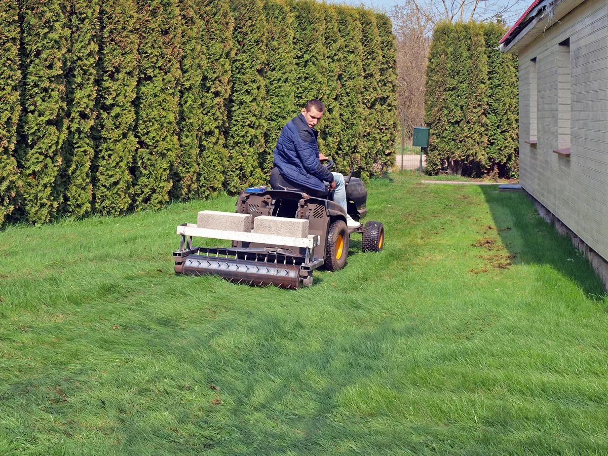 Young man working with lawn mower powered needle roller for soil aeration and moss removing