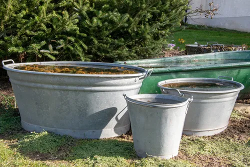 Three old zinc tubs and buckets in a garden. They are filled with water and are used as small garden ponds.