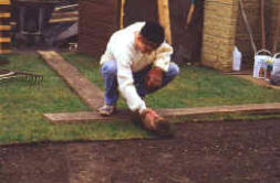 The scaffold boards in use with the roll of turf being laid